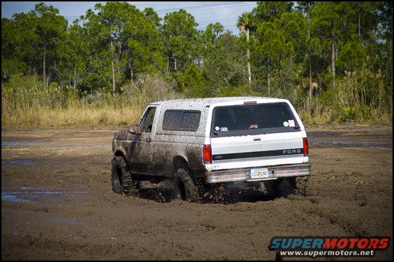 1996 Ford Bronco driving through mud, rear view. Mud covers the vehicle