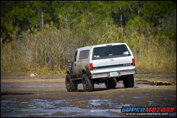 Ford Bronco driving through mud, rear view. Has a lift kit and off-road tires