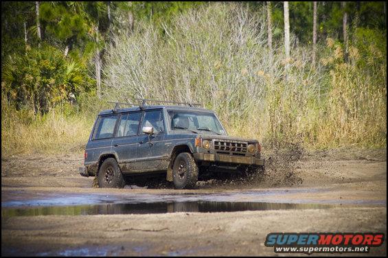 Dark SUV driving through mud and water, kicking up spray