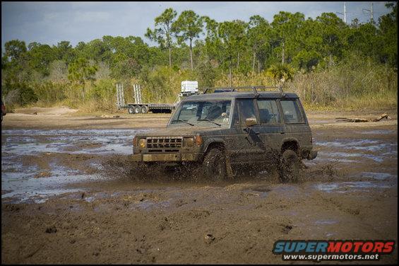Dark SUV splashing mud, front grille visible, roof rack, off-road tires