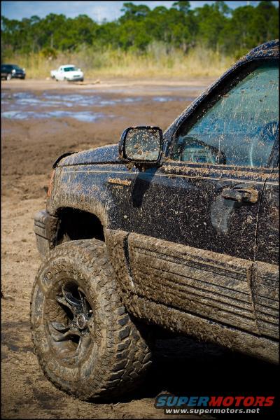 Mud-covered Jeep Grand Cherokee on a dirt track with other vehicles in the background