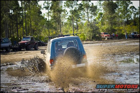 Blue SUV splashing through mud, spare tire on rear door