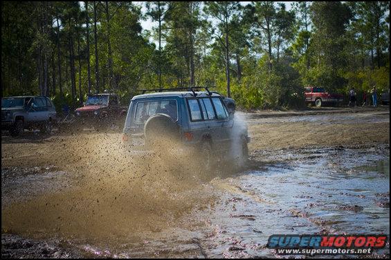 SUV driving through mud with other vehicles nearby