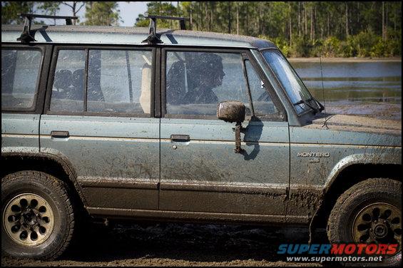 Mud-covered Mitsubishi Montero parked in shallow water, side view