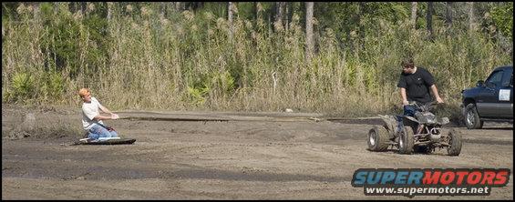 Quad bike with rider and a person on the ground, truck in background