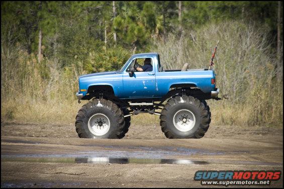 Blue monster truck with oversized tires driving on a dirt path