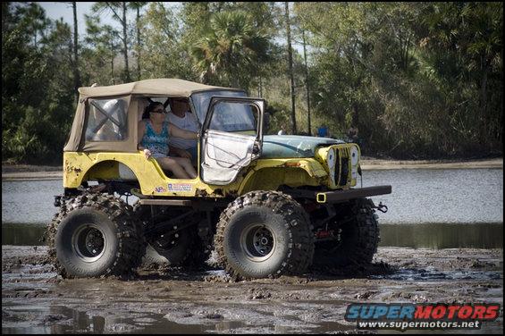 Yellow Jeep CJ-5 with large tires stuck in mud, two people inside