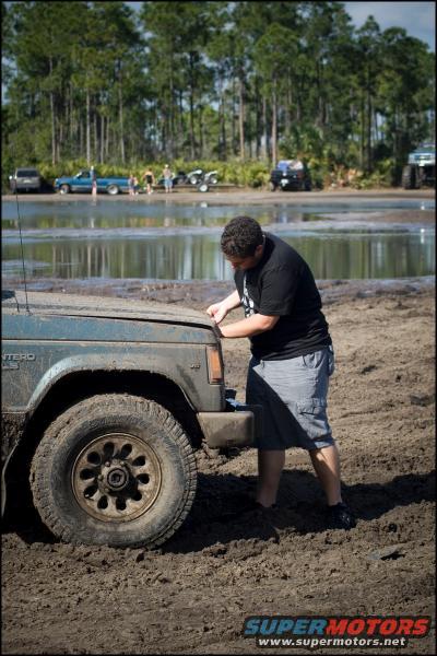 Blue SUV with hood open in mud, person checking engine