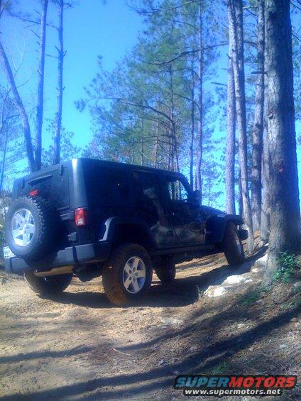 Black Jeep Wrangler on a dirt trail, rear spare tire visible, side view
