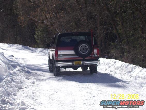 Red and white Ford Bronco with a spare tire on the back, driving on a snow-covered road