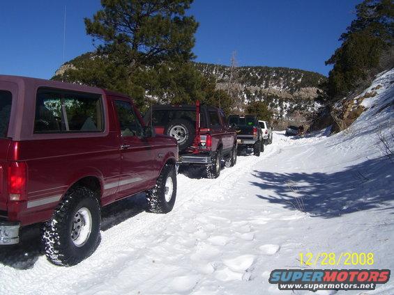 Red 1992 Ford Bronco in foreground, followed by other vehicles on a snow-covered road