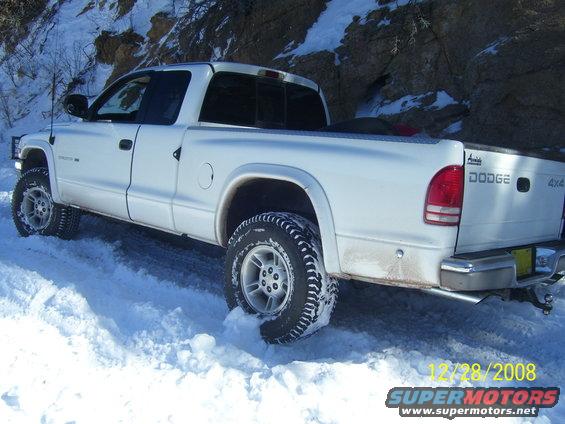 White Dodge pickup truck with off-road tires driving in snow