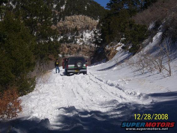 Rear view of a 1993 Ford Bronco on a snowy road with a person standing nearby