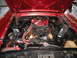 1972 Ford Ranchero - The engine bay of a red 1972 Ford Ranchero reveals a V8 engine with custom chrome and orange hoses.