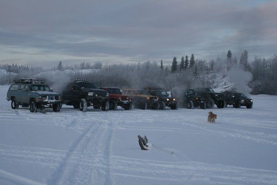 Light blue 1990 Chevrolet Suburban with roof rack in snow, next to other off-road vehicles