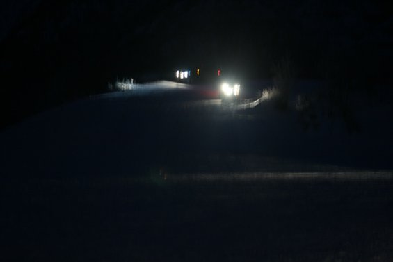 Several vehicles with headlights on drive on a snow-covered road at night