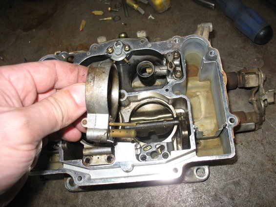 Hand holding part of a carburetor assembly, showing internal components and metal casing