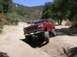 1996 Ford Bronco - A red SUV drives along a dirt path in a dry, wooded area, kicking up dust.