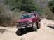1996 Ford Bronco - A red Ford Bronco navigates a dusty, off-road trail under a clear sky.