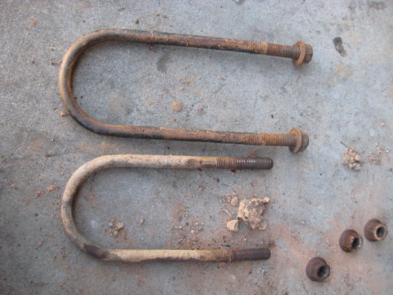 two rusted U-bolts with nuts, one larger than the other, lying on concrete