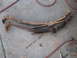 1978 Ford Bronco - Two aged leaf springs, one lighter and one darker, rest on a concrete floor with a red hose nearby.