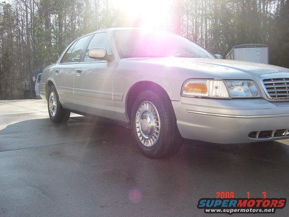 Silver 2000 Ford Crown Victoria sedan, front 3/4 view, chrome hubcaps, slight sun glare