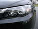 2008 Subaru Impreza - The front passenger side headlight of a black Subaru is shown, with a reflection of a house in the background. The page claims it's a 2008…