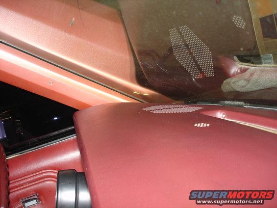Close-up of a car's red leather dashboard and windshield with speaker grilles.