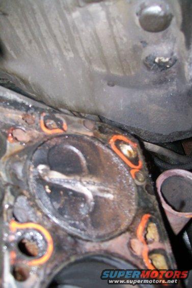 Engine cylinder head with orange gasket material visible around the cylinders. Some rust and debris are present