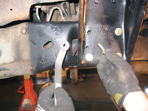 Gloved hands working on vehicle frame with jack stands visible