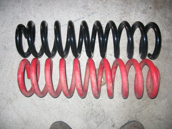 Two coil springs, one black and one red, laid on a concrete surface