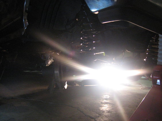 Underside of a vehicle on jack stands, with a bright light illuminating the suspension components
