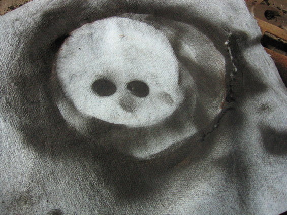 Skull stencil on dirty, textured fabric with circular spray paint marks