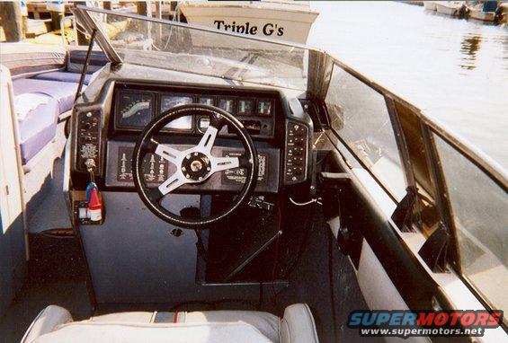 Boat interior with dashboard and steering wheel. Text on boat in background reads 'Trinle G's'