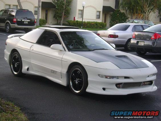 White 1994 Ford Probe with a grey aftermarket hood and custom side skirts, parked in a lot with other cars