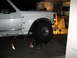 1996 Ford Bronco - Front wheel and fender of a white truck are visible while it's supported by jack stands in a garage.