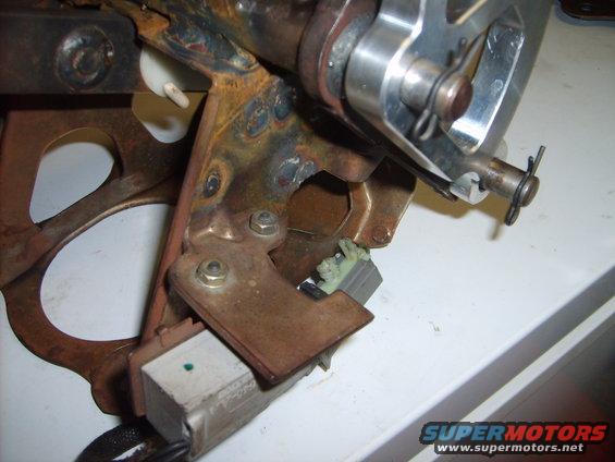 Close-up of rusty metal bracket and silver mechanism with a small green dot on a white block