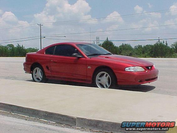 Red coupe parked on a concrete curb, viewed from the front three-quarter angle
