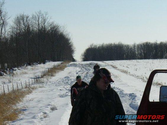 People on a snowy road with trees and a fence line