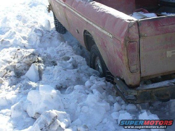 Red pickup truck with dented rear fender stuck in deep snow