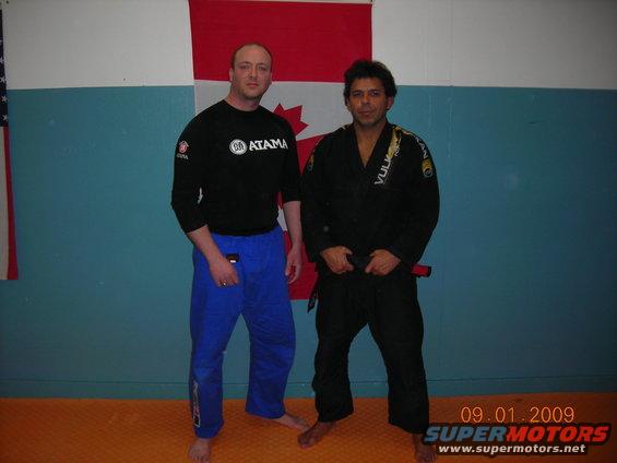 Two men in martial arts uniforms stand before Canadian and American flags