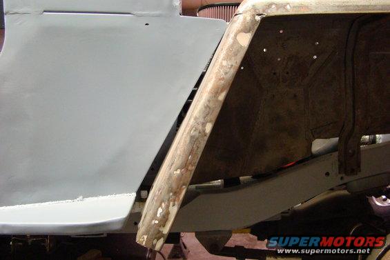 Close-up of a vehicle's body panel being repaired, showing primer on one side and rust and metal on the other