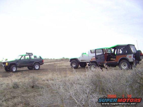 Three off-road vehicles parked on a dirt track with dry brush in the foreground
