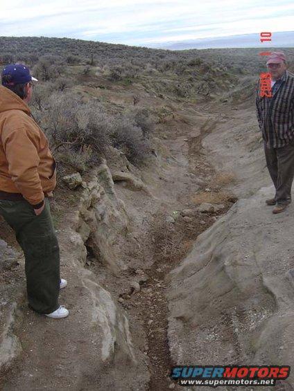 Two men observe a dry creek bed in a , arid landscape