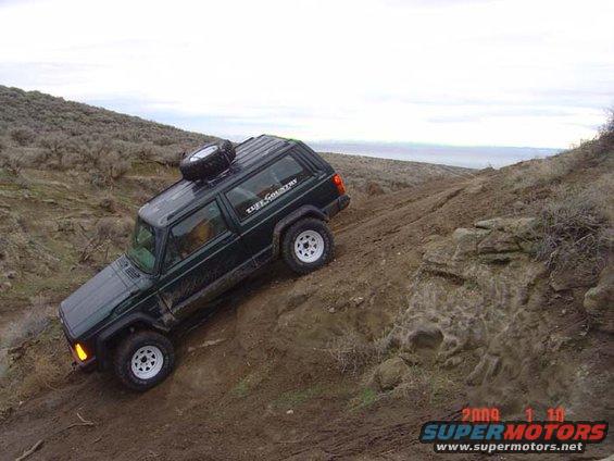 Green Jeep Cherokee XJ with 'Tuff Country' decal on side, driving up a dirt incline. Spare tire mounted on roof rack