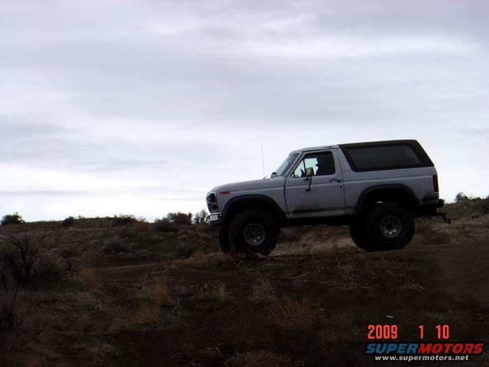 Silver Ford Bronco on a dirt hill under a cloudy sky