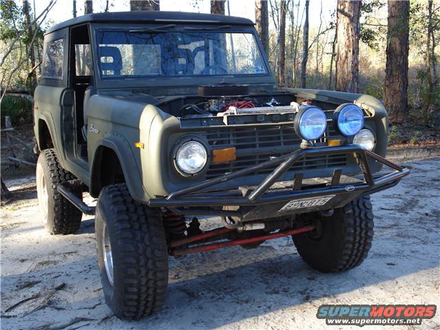 Green Ford Bronco with aftermarket bumper and lights. Engine is visible under the open hood
