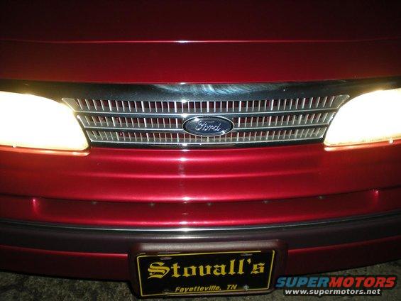 Red Ford Crown Victoria front end with chrome grille and Ford logo. Headlights are on