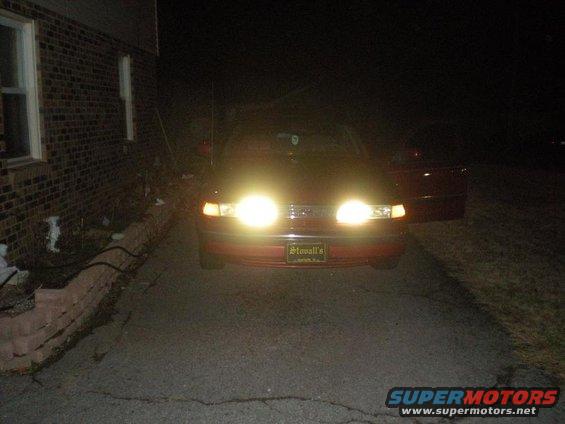 red sedan with headlights on, parked in driveway at night. License plate frame says "Stovall's"