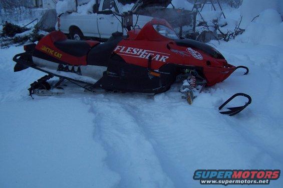 Red snowmobile with 'ARCTIC CAT' and 'FLESHGEAR' text in snow
